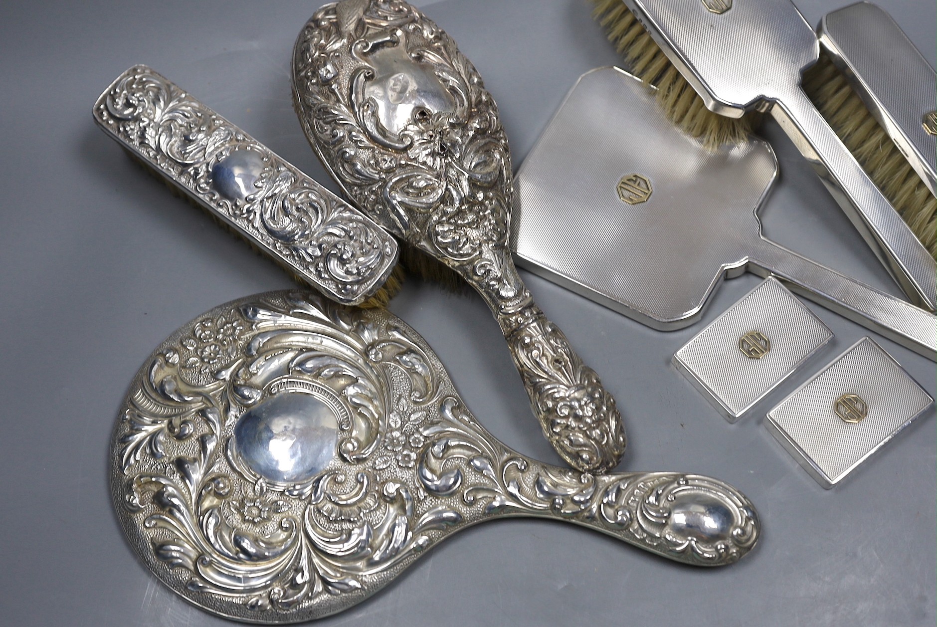 A 1970's engine turned silver three piece dressing table set, with a pair of matching jar lids, and a repousse decorated three piece dressing table set